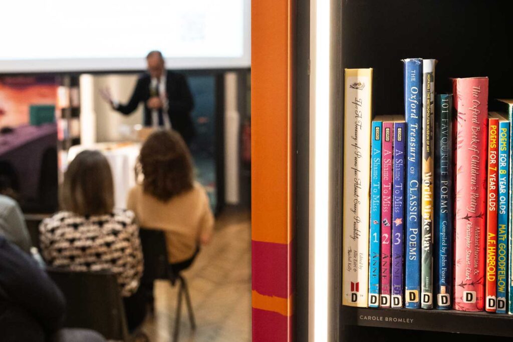 Close up image of library books with event host Anthony Horowitz in the background by event photographer Adam Hollingworth